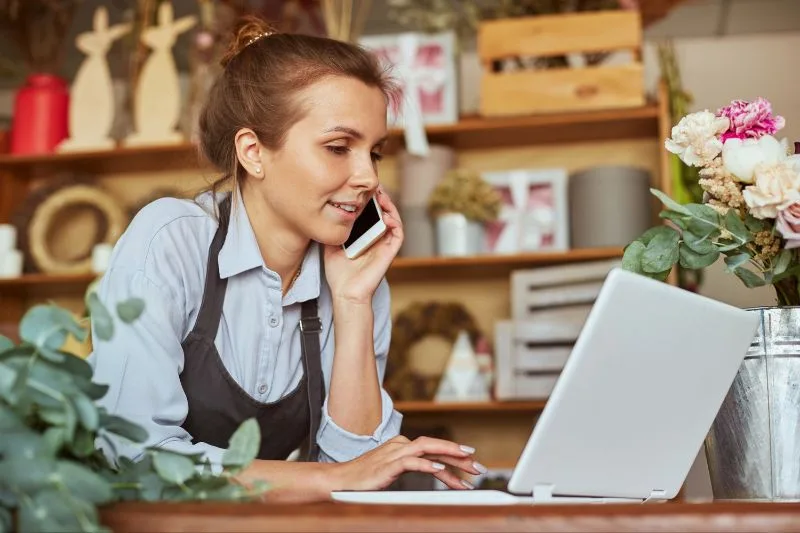 Mujer autónoma trabajando en su negocio, consultando información legal en su portátil mientras realiza una llamada.
