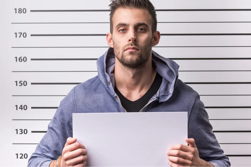 Hombre joven detenido en una comisaría con fondo de medidas de altura.