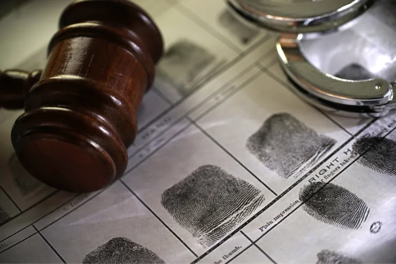 Martillo de juez sobre fichas dactilares y esposas, representando el proceso penal y la justicia.